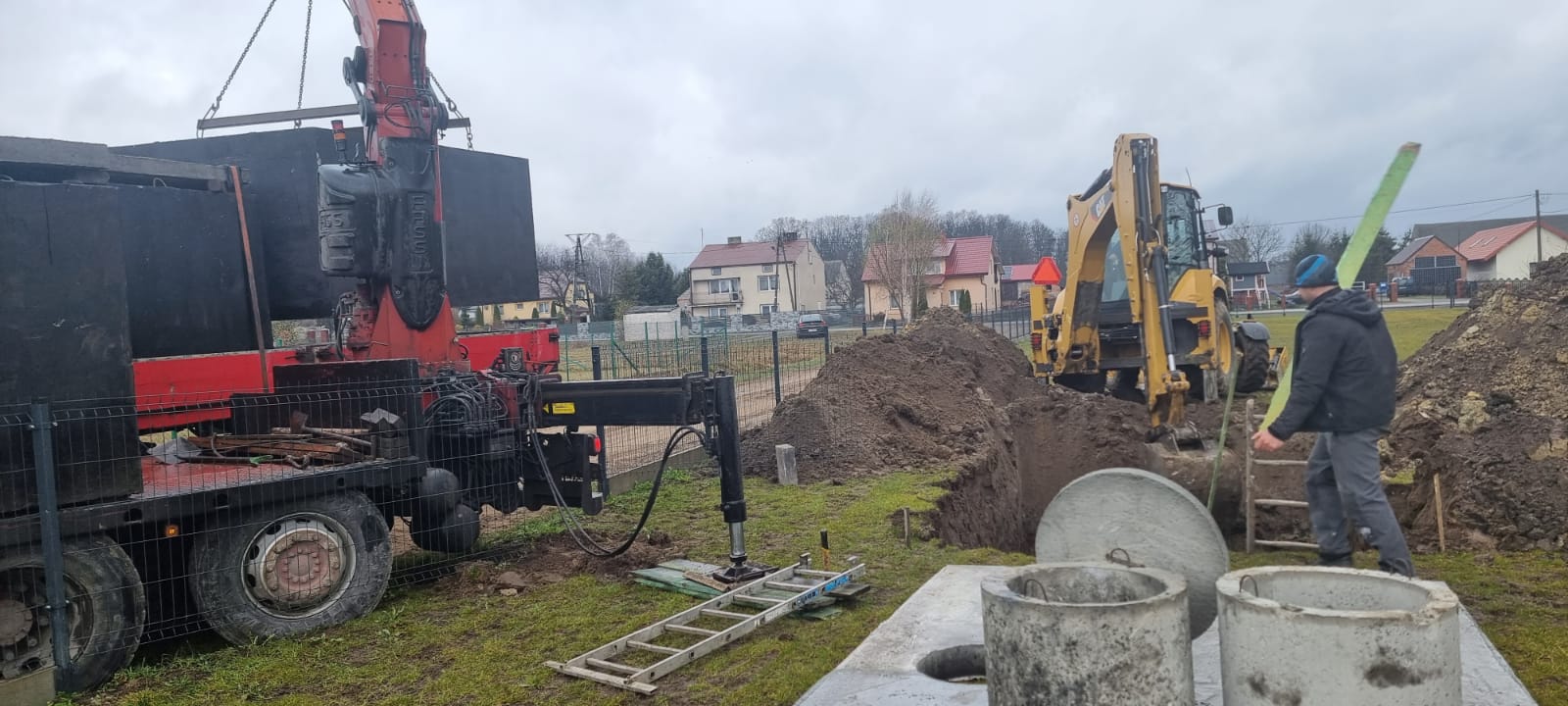 Wykop pod szambo w pobliżu zabudowań, obok zbiornik i sprzęt budowlany