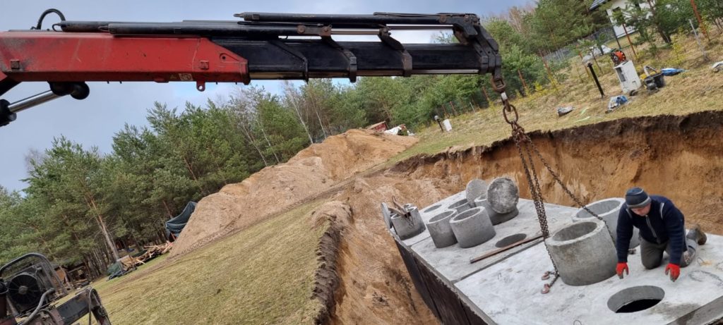 Zbiornik betonowy opuszczany dźwigiem do głębokiego wykopu, widoczne kręgi i włazy