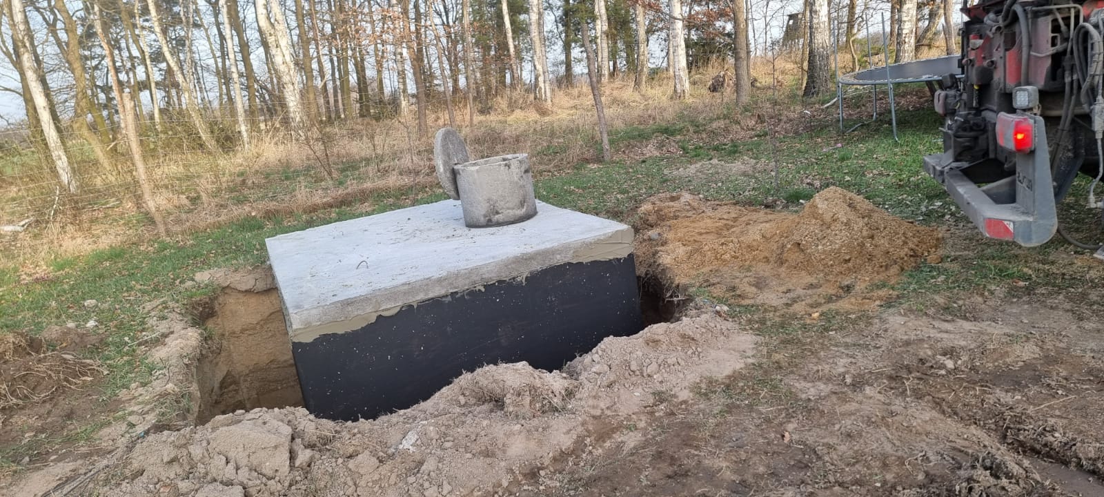 Betonowy zbiornik z włazem opuszczony do wykopu, obok hałdy ziemi